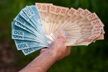 Close-up of adult hand holding bunch of Brazilian Reais notes of value 100 and value 50 with defocus background. Photo taken September 9th, 2025, Zurich, Switzerland.