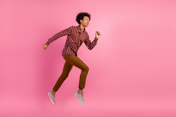 Excited young man in stylish casual wear jumping with joy against a vibrant pink background...