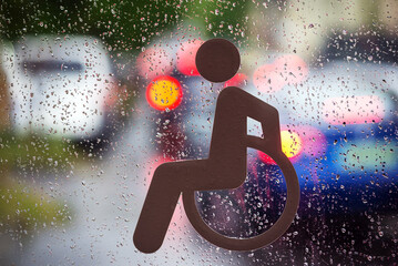 Symbol of person on a wheelchair on the glass against waterdrops and traffic lights