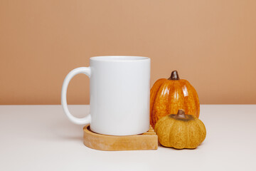 White mug mockup on ceramic cup coaster with pumpkins. Mockup coffee or tea mug for autumn design, gift, logo or print
