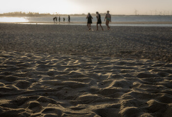 Sunset light over sandy beach with people walking