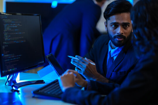A lead software architect mentors a junior developer, explaining a complex codebase. They are engaged in a pair programming and knowledge transfer session in a high-tech data center.