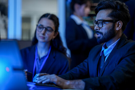 A lead software architect mentors a junior developer, explaining a complex codebase. They are engaged in a pair programming and knowledge transfer session in a high-tech data center.