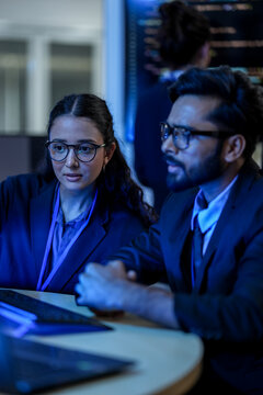 A lead software architect mentors a junior developer, explaining a complex codebase. They are engaged in a pair programming and knowledge transfer session in a high-tech data center.