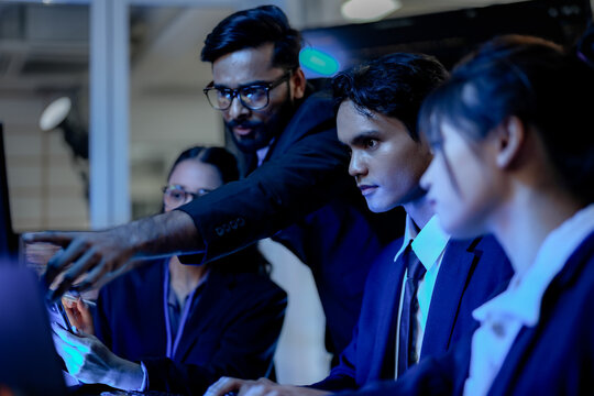 A lead software architect mentors a junior developer, explaining a complex codebase. They are engaged in a pair programming and knowledge transfer session in a high-tech data center.
