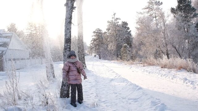 Happy child girl shaking snowy tree making snowfall, cool attitude. Outdoors winter activities for kids. December landscape, nordic country