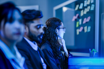 An agile development team participates in a sprint retrospective meeting. A female developer contemplates the user stories on the kanban board visible in the background.