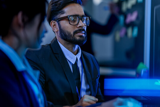 An agile development team participates in a sprint retrospective meeting. A female developer contemplates the user stories on the kanban board visible in the background.