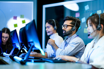 A team leader trains a new customer service agent in a modern call center. The diverse team works together to provide professional and helpful technical support to clients.