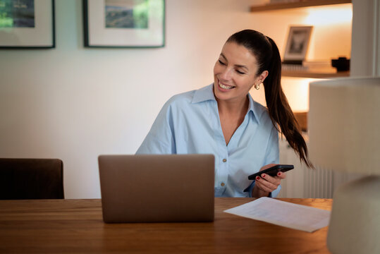Middle-aged woman sitting at home and using laptop and smartphone for work