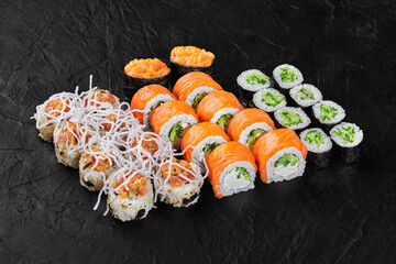 Sushi set displayed on black slate featuring salmon, cucumber, and various toppings