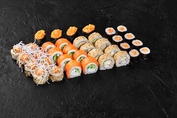 Sushi set displayed on black background featuring variety of rolls