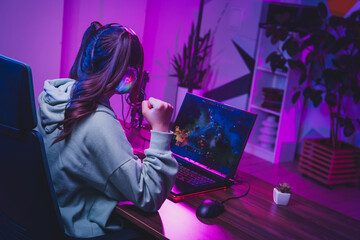 Young female gamer in headphones streaming video games on laptop in neon-lit room during nighttime © deagreez