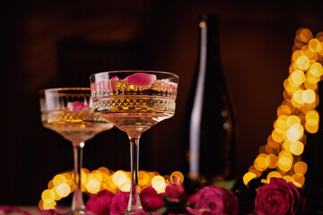 Crystal champagne glasses with pink roses and golden fairy lights, creating an elegant and romantic celebration atmosphere.