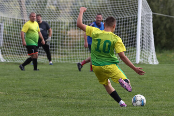 A footballer in a yellow and green uniform kicks the ball in front of the goal