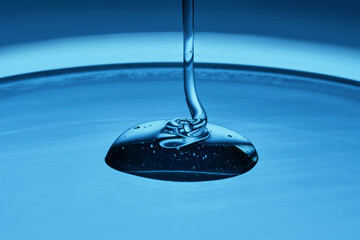 The viscous gel serum for the face flows and collects into a drop on a blue background..
