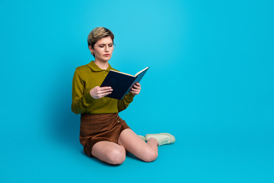 Young woman with trendy short hair reading a book against a vibrant blue backdrop, showcasing casual style and focus.