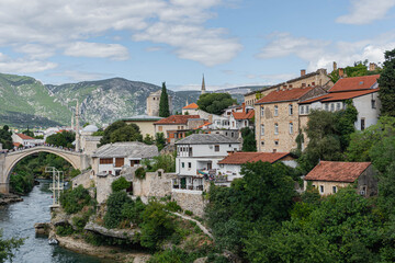 view of the old town of mostar with many mosque minarets and very famous old bridge most with neretva clear river flowing under it on cloudy day