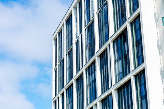 The building's façade is modern in style, with large rectangular windows arranged in a strict geometric pattern. The white frames contrast with the dark glass, and the blue sky is in the background.