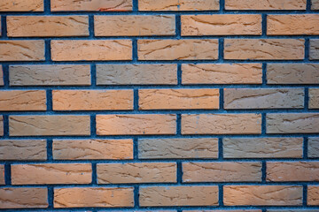 Obraz premium The brick wall is made of red-orange bricks with a clear texture. The joints between the bricks are filled with blue mortar, creating a contrast. The masonry is even, with a classic offset of rows.