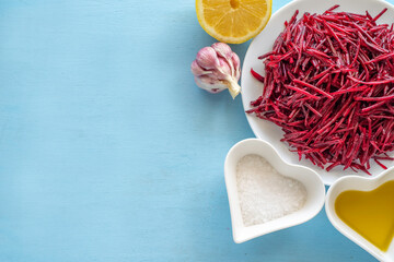 Ingredients for making marinated beetroot on blue wooden background. Fresh lemon, grated beetroot, garlic, salt over wooden surface.
