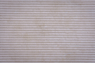 A textured stone surface with evenly spaced horizontal ridges forms a rhythmic pattern. The...