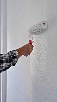 Close-up of a hand. A painter paints a masonry wall with white paint using a roller. Construction industry. 