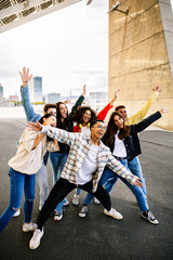 Multi-ethnic group of young students celebrating together outdoors, joyfully raising arms and...