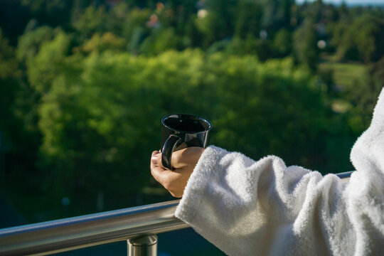 A girls hand holding a cup of coffee on a balcony, overlooking a parking lot and trees, a concept of morning routine, urban life, and leisure.