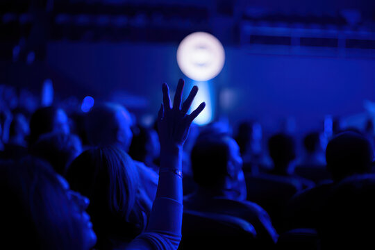 Audience member raises hand in a dark concert venue with blue lighting - Powered by Adobe