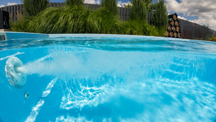 Powerful water jet bubbles underwater in a backyard swimming pool, surrounded by lush greenery and...