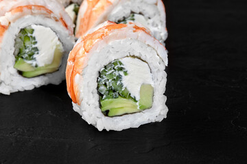 Sushi rolls with shrimp, avocado, cucumber, cream cheese and rice lying on dark background