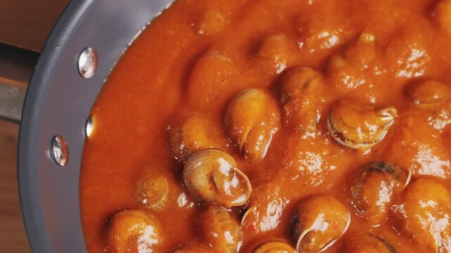 French snails, Close up of traditional spanish tapas - the boiled snails in tomato sauce with garlic and chili in black iron pan