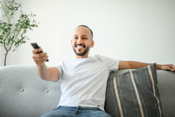 young islamic arab man relaxing on sofa at home watching tv