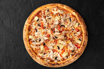 Delicious pizza with chicken, pineapple, and mushrooms resting on black surface