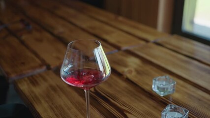 closeup of hand gently dropping ice cube into wine glass filled with red drink on polished wooden table with natural daylight streaming through window creating warm ambient indoor setting - Powered by Adobe