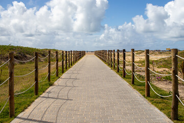 Fototapeta premium Caminho para a Praia com Céu Azul e Nuvens – Passarela de Madeira e Corda nas Dunas de Areia