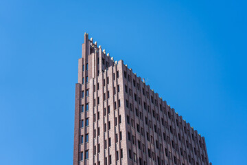 Fototapeta premium A red brick high-rise stands against a bright blue sky. Its architecture appears angular and massive.