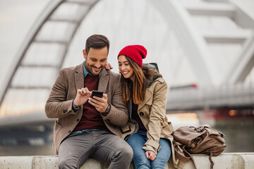 Couple enjoys time together sharing laughter while checking mobile phone outdoors near urban bridge