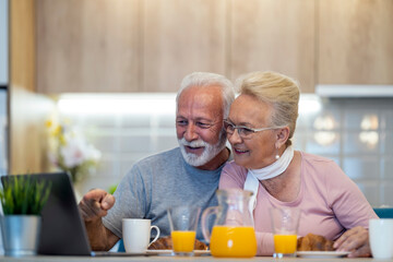 Elderly couple enjoys sharing laughter and stories while using a laptop at home during a sunny morning