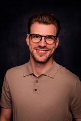Obraz premium Headshot of a young man looking at camera and smiling against isolated dark background