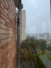 Rainy day cityscape view through window with raindrops on glass and brick wall creating moody atmosphere