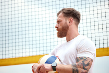Man with tattoo holding volleyball near net on sunny day