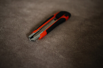 Utility knife with retractable blade lying on soft textured surface. Concept of construction tools, repair, DIY projects, cutting equipment, and everyday household items