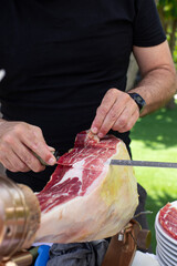 Man slicing traditional Iberian ham by hand with a long knife at an outdoor event

