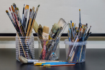 Various professional used paint brushes in the jars on a dark surface