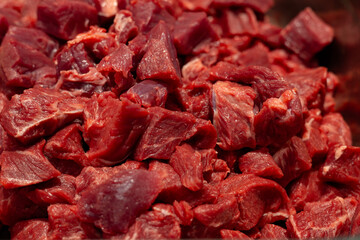 Close-up of fresh, raw beef cut into cubes. A butcher prepares uncooked meat by slicing it into...