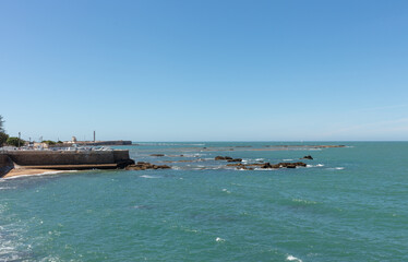 Coastal view with rocky shore and fortress in the distance. Cadiz, Andalusia, Spain, September 2025.