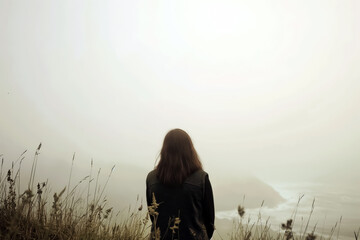 Solitary woman sitting in nature facing foggy landscape and sea view