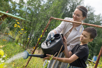 Caucasian woman and her son watering flowers in the garden. 